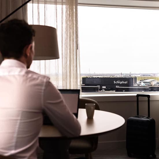 Man working at a desk with a view of Schiphol Airport from a hotel window